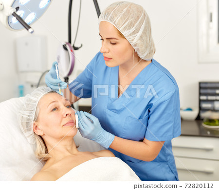 Senior woman getting injection for facial rejuvenation procedure in esthetic clinic 72820112