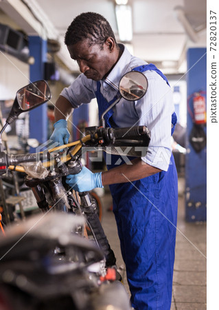 Service engineer repairs a motorcycle steering wheel in a motorcycle service Service engineer repairs a motorcycle steering wheel in a motorcycle service 72820137