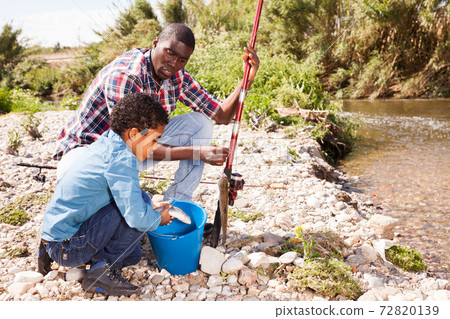 Boy and his father holding fish on hook Boy and his father holding fish on hook 72820139