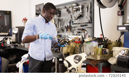 Confident worker examines a broken motorcycle part of the working area 72820145
