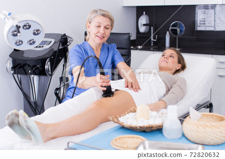 Beautician performing machine cosmetological procedure Beautician performing machine cosmetological procedure 72820632