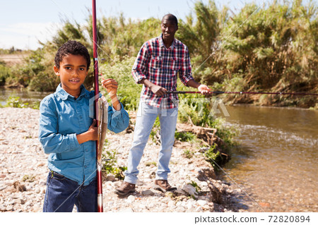 Man and boy holding fish on rod Man and boy holding fish on rod 72820894