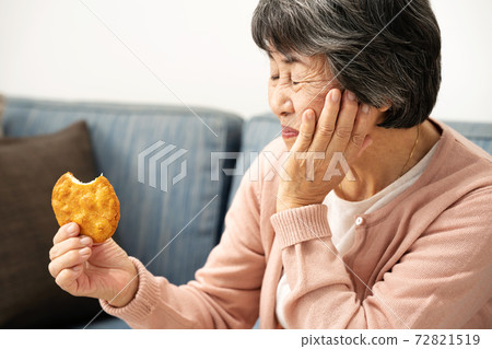 Senior woman eating rice crackers 72821519