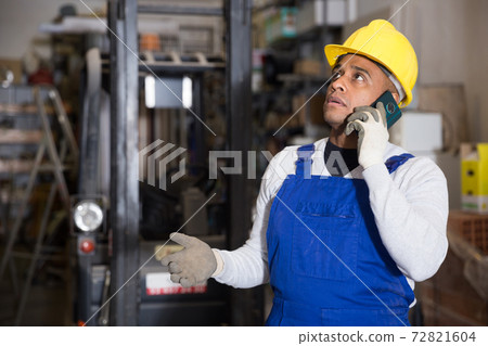 Focused worker of building materials warehouse talking on phone 72821604