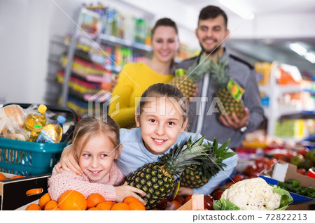 Smiling little girls choosing fresh fruits while shopping with parents 72822213