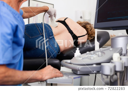 Elderly man sonographer using ultrasonography machine checking female patient in hospital diagnostic room Elderly man sonographer using ultrasonography machine checking female patient in hospital diagnostic room 72822283