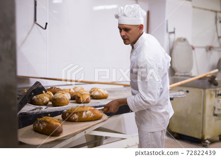 Baker takes out hot bread from oven 72822439