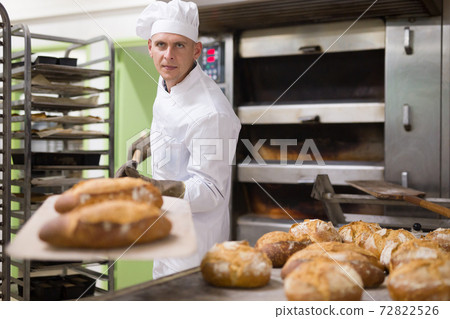 male baker with bread on baking shovel in kitchen 72822526