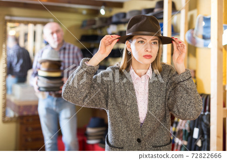 Woman fitting on classic hat in shop Woman fitting on classic hat in shop 72822666