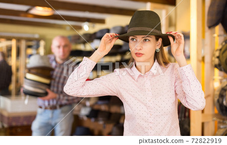 Woman fitting on classic hat in shop Woman fitting on classic hat in shop 72822919