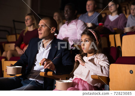 Dad and daughter carefully watch a movie in cinema hall Dad and daughter carefully watch a movie in cinema hall 72823085