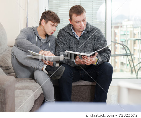 Father helps son solve school assignments Father helps son solve school assignments 72823572