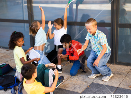 Cheerful preteens resting outdoors in schoolyard during break Cheerful preteens resting outdoors in schoolyard during break 72823646