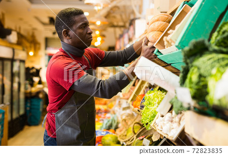 Seller arranging squash on greengrocery counter 72823835