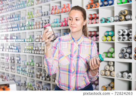 portrait of woman choosing paint color in aerosol can in art shop 72824263