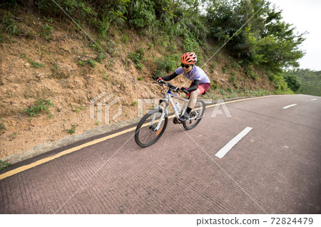 Woman riding bike down a slope with fast speed on mountain trail 72824479