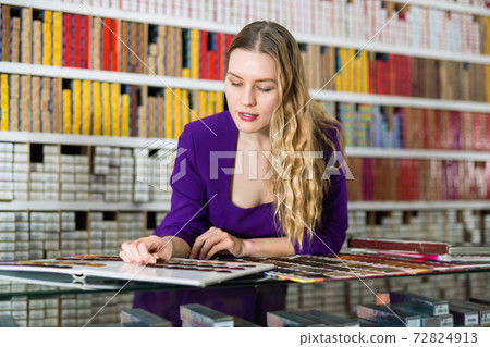 Interested attractive girl looking at palette of hair colors in cosmetics store Interested attractive girl looking at palette of hair colors in cosmetics store 72824913