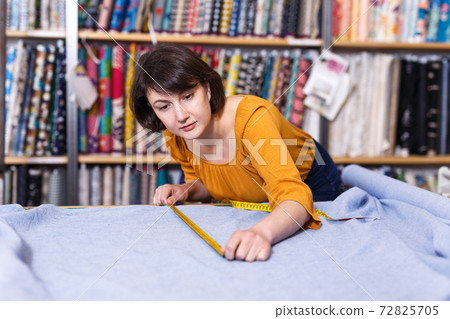 Female seller measuring and cutting off piece of textile Female seller measuring and cutting off piece of textile 72825705