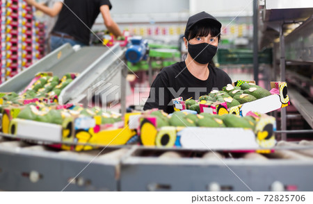 Woman in mask carrying box with avocados Woman in mask carrying box with avocados 72825706
