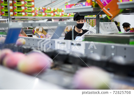woman with box stands near a conveyor belt with mango woman with box stands near a conveyor belt with mango 72825708