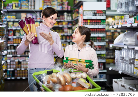 smiling woman customer with girl looking for pasta in supermarket smiling woman customer with girl looking for pasta in supermarket 72825709