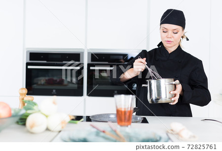 Positive female cook with whisk, team working on kitchen 72825761
