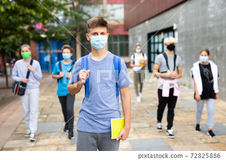 Young student in a protective mask going to college down city street Young student in a protective mask going to college down city street 72825886