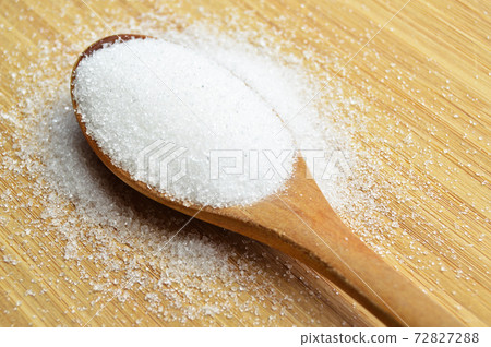 Granulated sugar in wooden spoon on bamboo cutting board, on bamboo cutting board 72827288