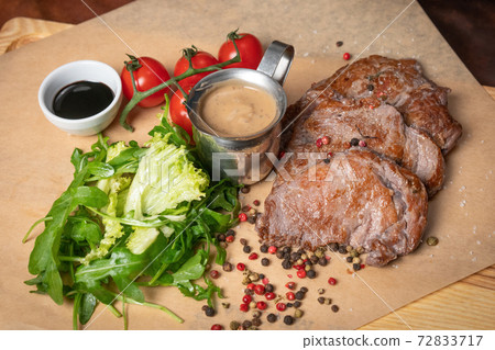 Pork fillets are served with barbecue sauce, soy sauce, cherry tomatoes, lettuce salad with arugula-seeded pepper mixture. Restaurant concept. Restaurant food. Grill concept 72833717