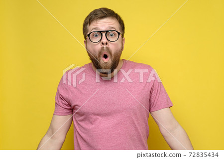 Man with glasses in shock, he opened mouth in surprise, looks with big eyes and spreads arms to the 72835434