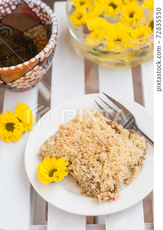 piece of cake with crumbs, tea and yellow flowers on white wooden background 72835550