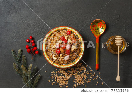 kutya, porridge made from spelt, with nuts, berries and honey. On a black background with a painted wooden spoon. Top view with space 72835986