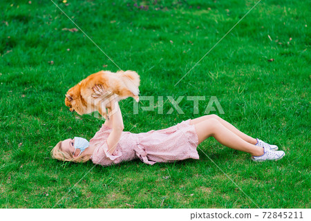 Young beautiful female in a blue mask with a dog on a background of a blossoming tree. 72845211