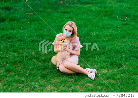 Young beautiful female in a blue mask with a dog on a background of a blossoming tree. 72845212