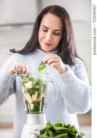 Last leaves of greens being put into a mixer by a gorgeous young woman Last leaves of greens being put into a mixer by a gorgeous young woman 72849367