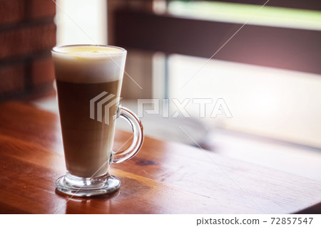 Large glass cup of coffee on a wooden table by the window 72857547