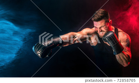 Bearded tattooed sportsman muay thai boxer in black undershirt and boxing gloves fighting on dark background with smoke. Bearded tattooed sportsman muay thai boxer in black undershirt and boxing gloves fighting on dark background with smoke. 72858705