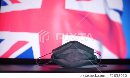 Disposable medical mask against flag of the United Kingdom. British COVID-19 outbreak concept Disposable medical mask against flag of the United Kingdom. British COVID-19 outbreak concept 72858910