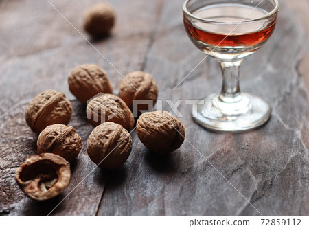 Walnut liquor in glass and walnuts on the old wooden background in backlight Walnut liquor in glass and walnuts on the old wooden background in backlight 72859112