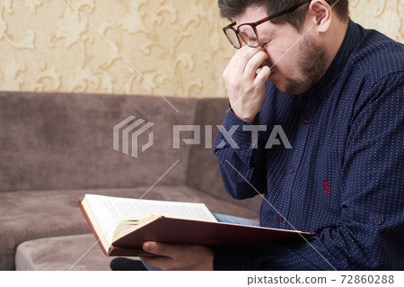 Concept, Caucasian man wearing glasses has sore eyes while reading a book, copies of space Concept, Caucasian man wearing glasses has sore eyes while reading a book, copies of space 72860288