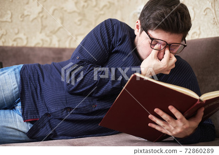 Concept, Caucasian man wearing glasses has sore eyes while reading a book, copies of space 72860289