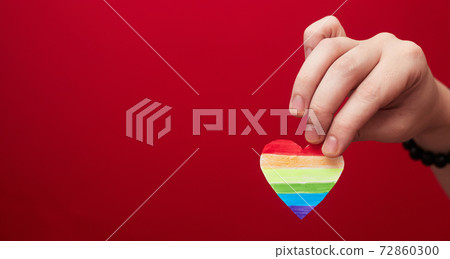 Lgbt valentine's day concept, rainbow heart in hand on red background, copy space Lgbt valentine's day concept, rainbow heart in hand on red background, copy space 72860300