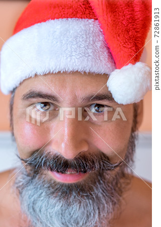Close-up portrait of smiling, well tanned, bearded caucasian man in a Santa Claus hat standing in front of cacti on the beach. Close-up portrait of smiling, well tanned, bearded caucasian man in a Santa Claus hat standing in front of cacti on the beach. 72861913