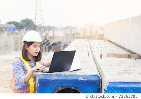 Beautiful Asian female engineer in white safety hard hat using laptop computer notebook doing job at construction site outside office. Idea for modern working woman. Beautiful Asian female engineer in white safety hard hat using laptop computer notebook doing job at construction site outside office. Idea for modern working woman. 72863793