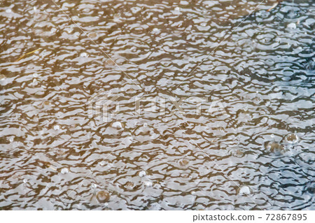 Puddle of water with splashing raindrops during a downpour Puddle of water with splashing raindrops during a downpour 72867895