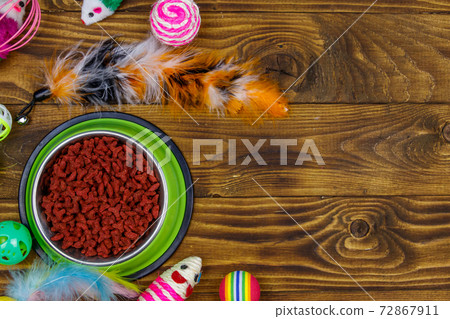Set of toys for cat and bowl with dry pet food on wooden background. Top view, copy space. Pet care concept 72867911