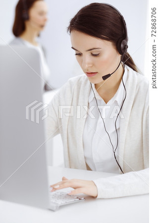 Call center. Casual dressed woman sitting in headset at customer service office. Group of operators at work. Business concept Call center. Casual dressed woman sitting in headset at customer service office. Group of operators at work. Business concept 72868706