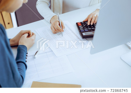 Accountant checking financial statement or counting by calculator income for tax form, hands close-up. Business woman sitting and working with colleague at the desk in office. Audit concept Accountant checking financial statement or counting by calculator income for tax form, hands close-up. Business woman sitting and working with colleague at the desk in office. Audit concept 72868745