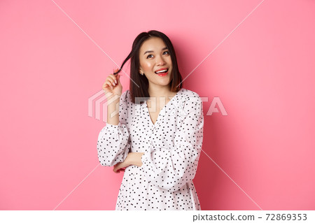 Dreamy cute asian girl thinking, imaging shopping and smiling, looking upper left corner with thoughtful smile, standing in dress over pink background 72869353