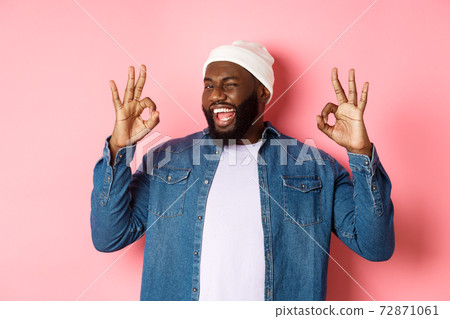 Satisfied african-american man in hipster beanie, showing okay signs in approval, praising good offer and saying yes, smiling pleased, standing over pink background 72871061